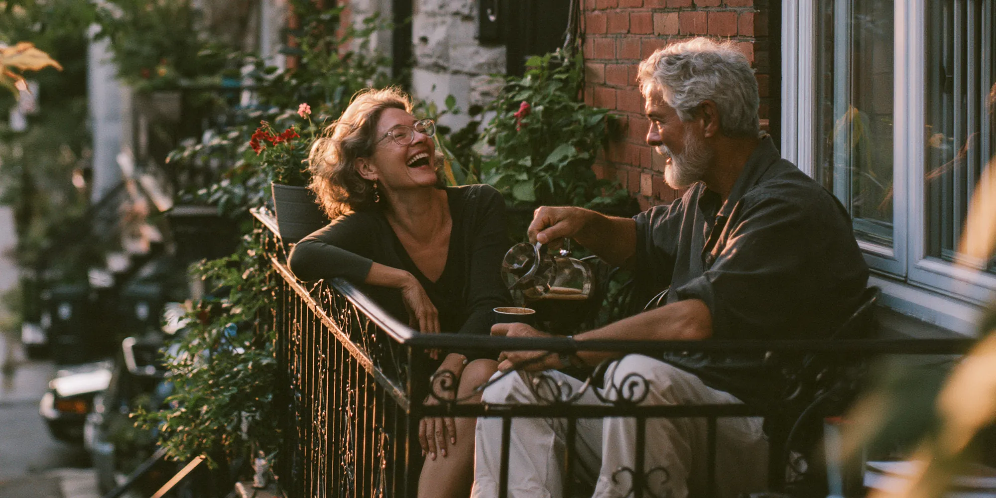 Couple de retraités qui rit sur le balcon fleuri de sa maison en brique