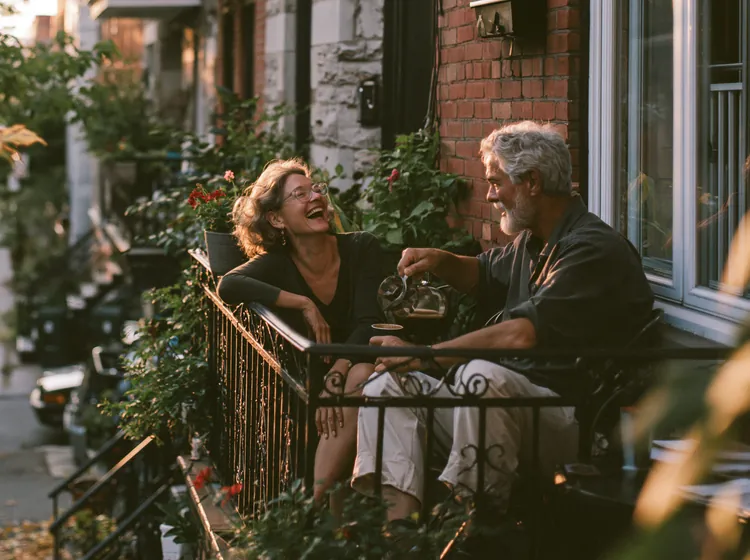 Couple de retraités qui rit sur le balcon fleuri de sa maison en brique