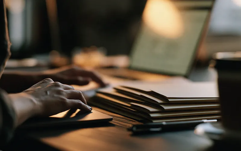 Mains sur un ordinateur portable à côté d’une pile de dossiers, pendant la comparaison des prêteurs