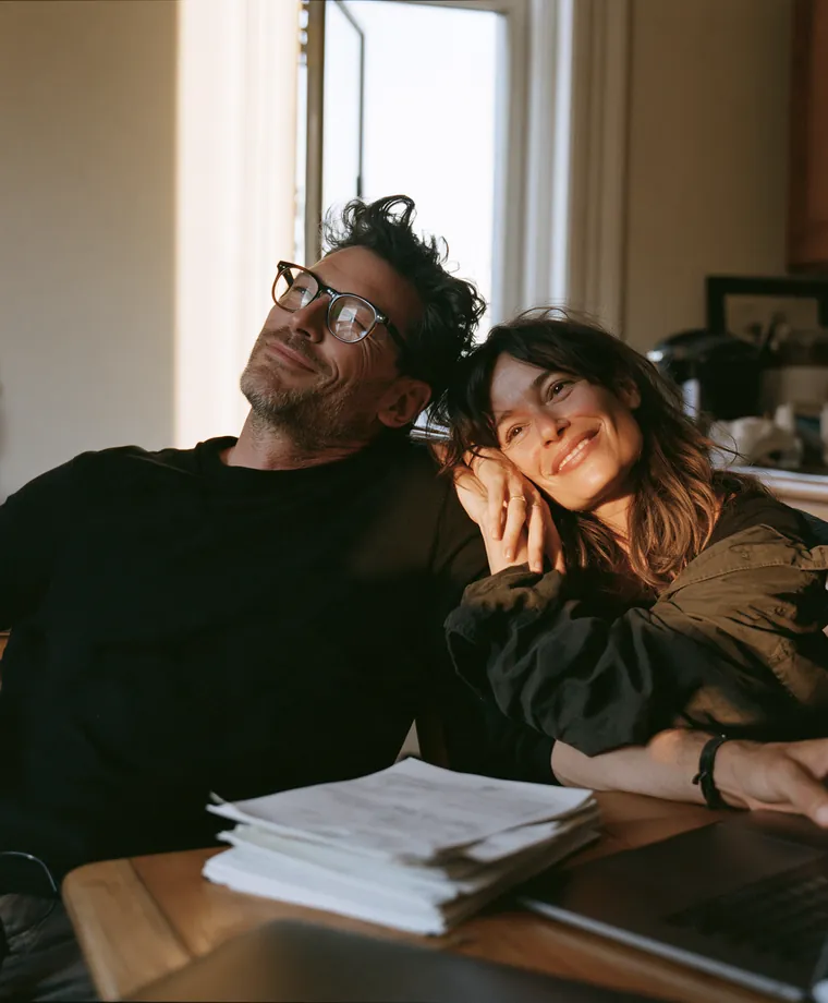 Couple souriant et soulagé à sa table de cuisine, une pile de factures réglées devant lui