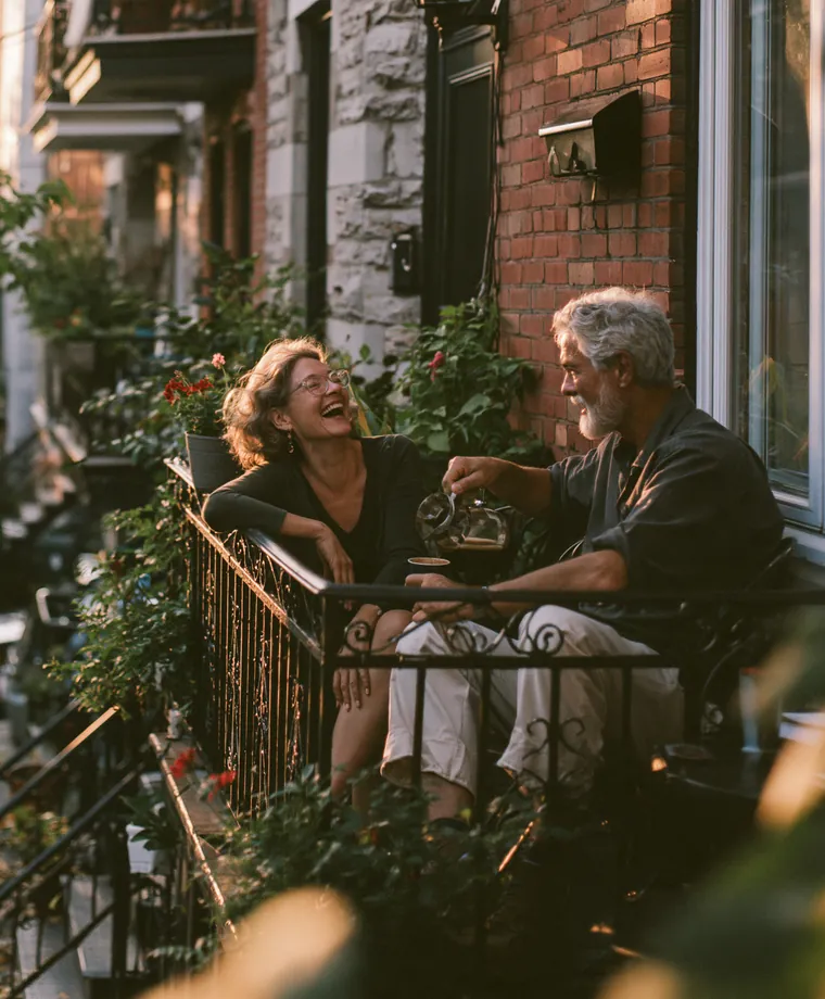 Couple de retraités qui rit sur le balcon de sa maison en brique