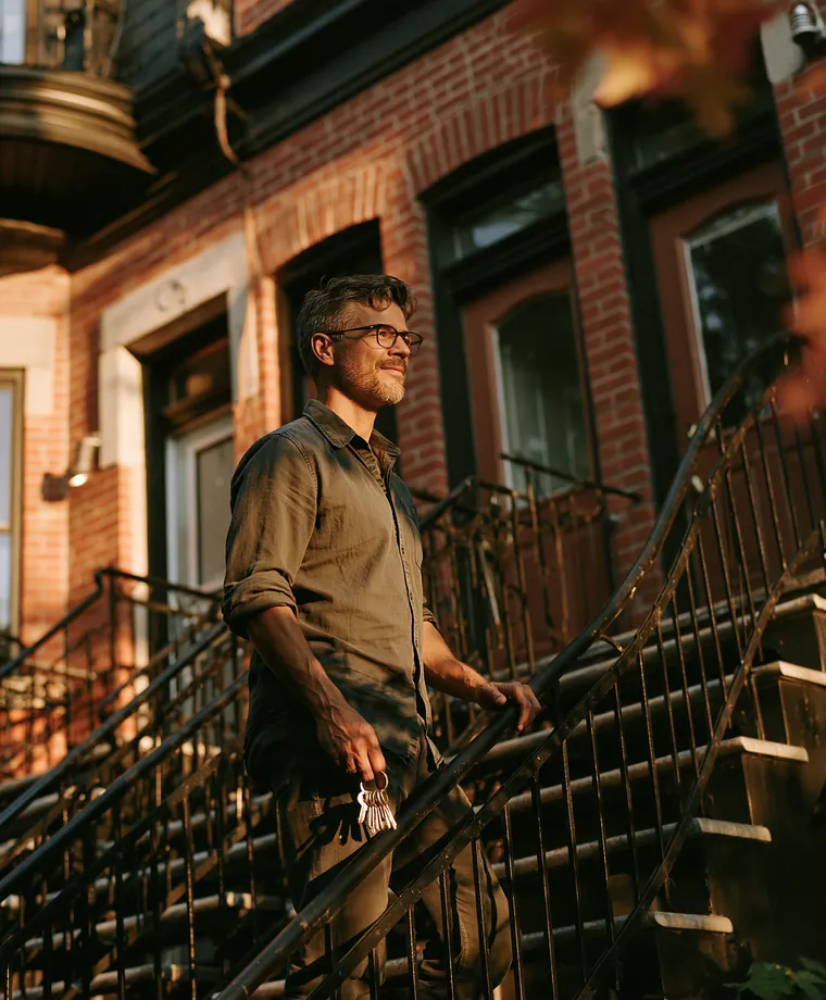 Propriétaire debout dans l’escalier extérieur de son plex montréalais, clés à la main